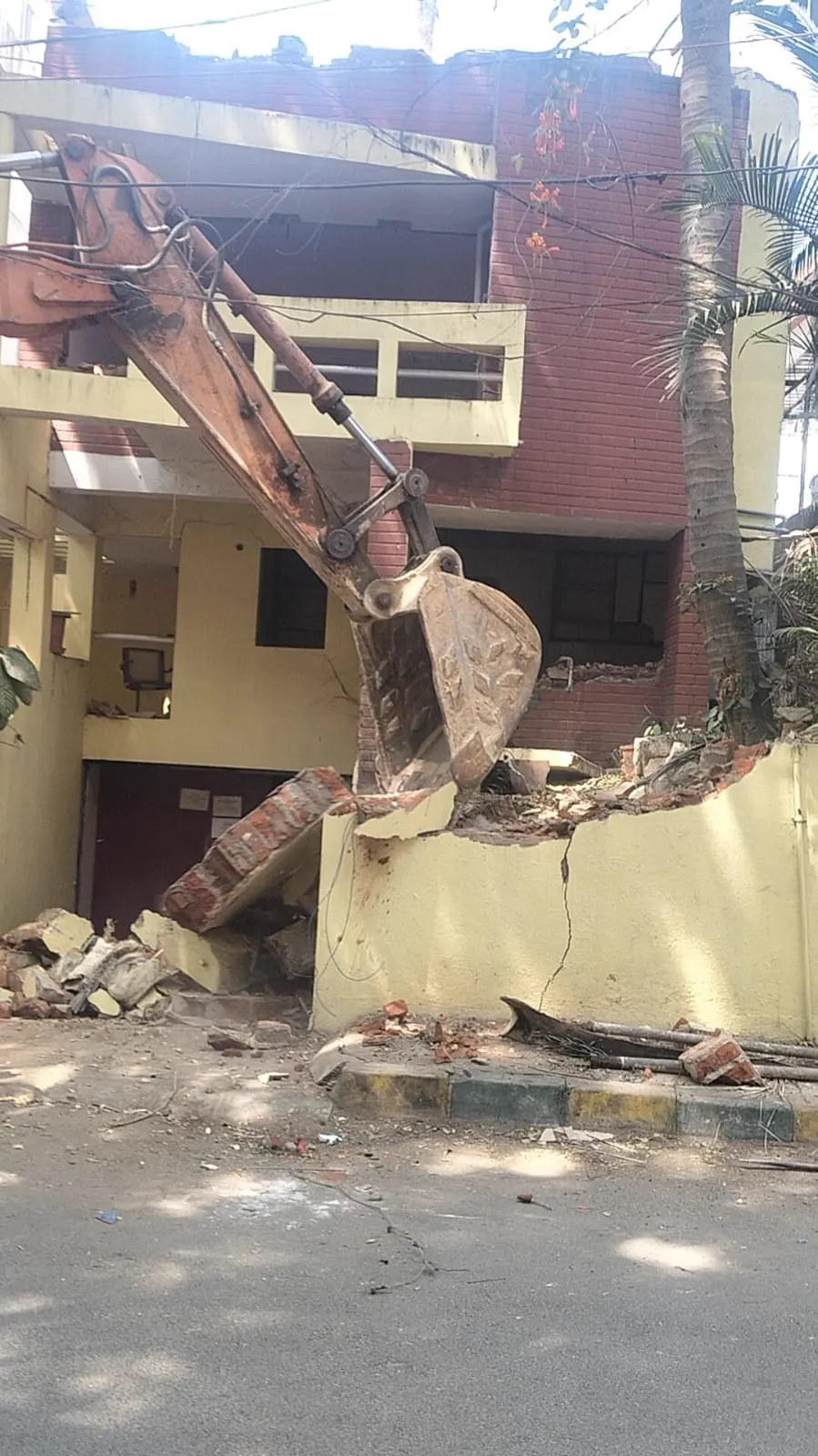 Excavator demolishing residential building wall in Bangalore